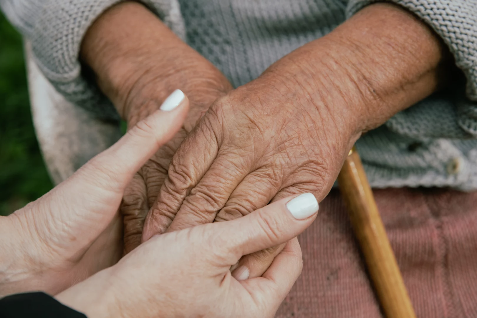 A caregiver holding the hand of an elderly woman.